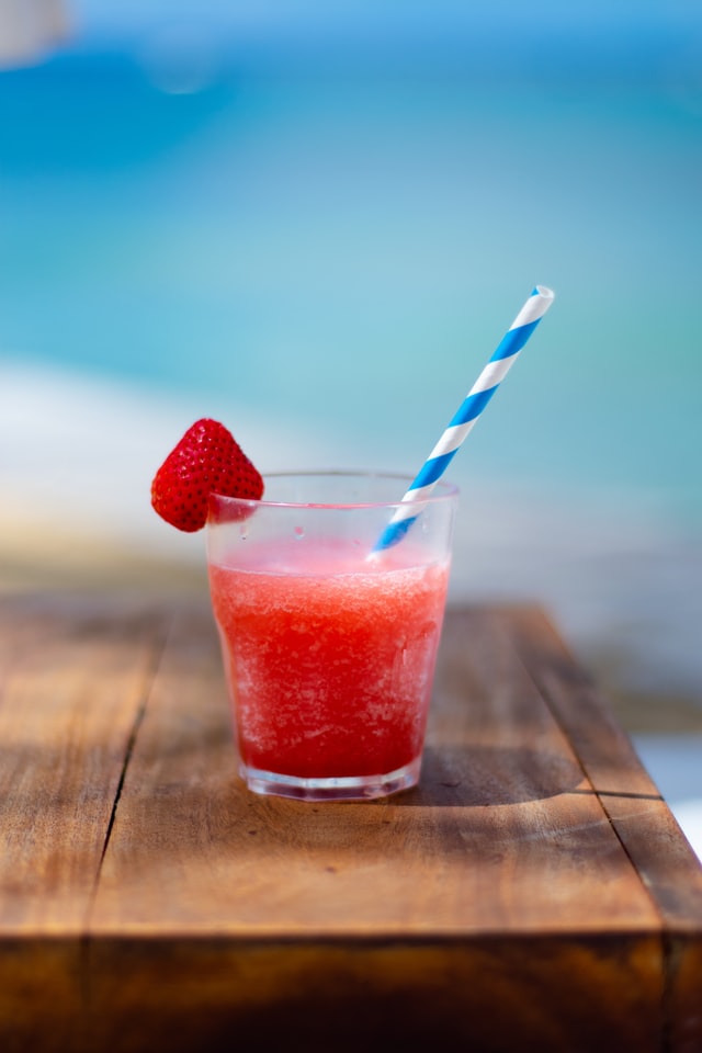 Strawberry daquiri with a big white and blue straw and strawberry on the rim.