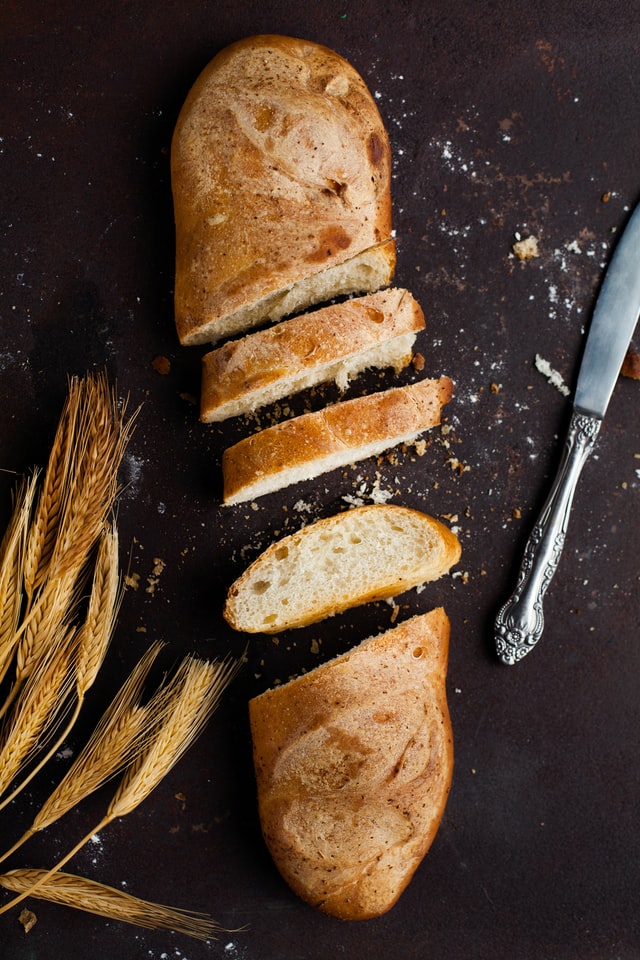 Sliced french bread next to butter knife and decorative grain.